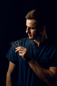 手术剪刀摄影照片_英俊的医生在深色背景上用手术剪刀。