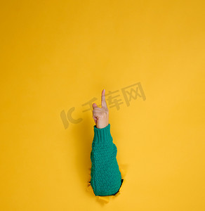 女性手从黄色纸背景中的破洞中伸出，身体的一部分用食指指向顶部。