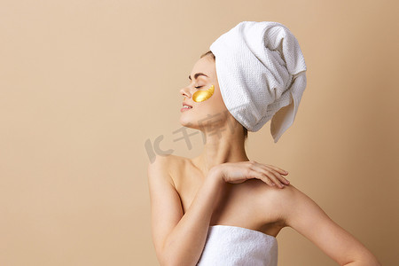 年轻女子脸上有金色斑块，头上有一条毛巾，米色背景