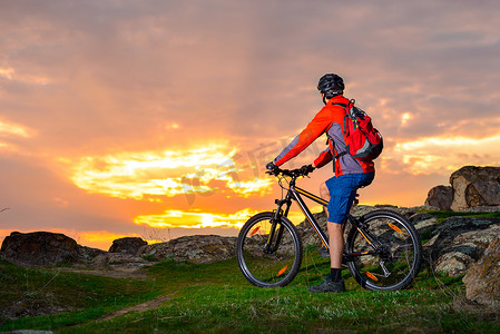 骑自行车的人骑着山地自行车在春天的岩石小道上欣赏美丽的日落。
