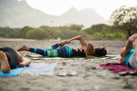 在毛里求斯印度洋空荡荡的海滩上，妇女们在背景山上做瑜伽练习或支撑鸽子姿势。