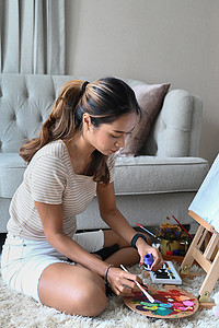 富有创造力的年轻女子坐在画架前，用水彩画画。