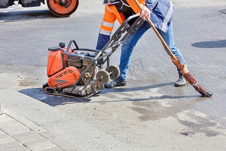 道路工人使用汽油振动压实机、振动压路机和旧扫帚在一段道路上压实沥青。