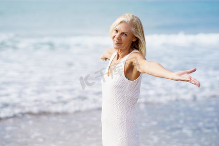 成熟女性在沙滩上张开双臂，度过闲暇时光，享受闲暇时光