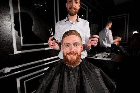 剪头发摄影照片_师父在理发店剪头发和胡须。