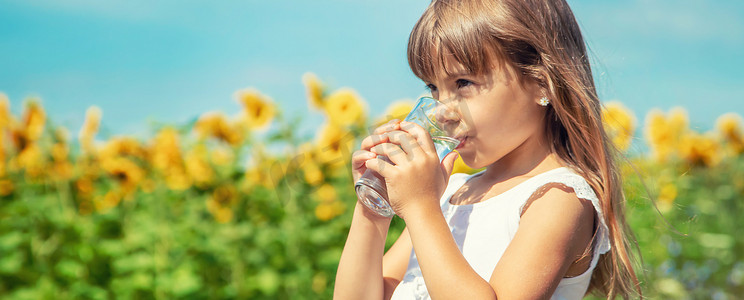 一个孩子在田野的背景下喝水。