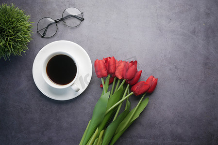 平面组合物咖啡、郁金香花和黑色背景上的眼镜。