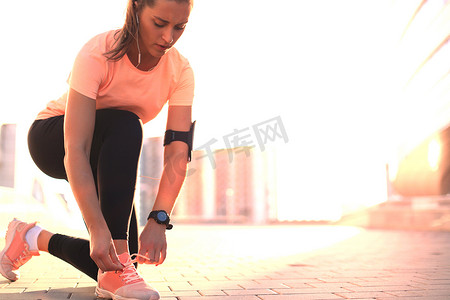 年轻健身迷人的运动型女跑步者将鞋带绑在她准备跑步的运动鞋上