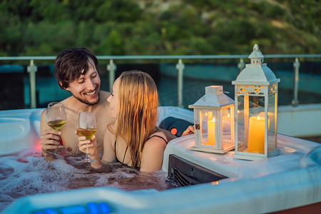 浴缸背景摄影照片_年轻无忧无虑的快乐微笑夫妇在绿色大山背景下享受快乐旅行时刻假期生活时在热水浴缸中放松的肖像