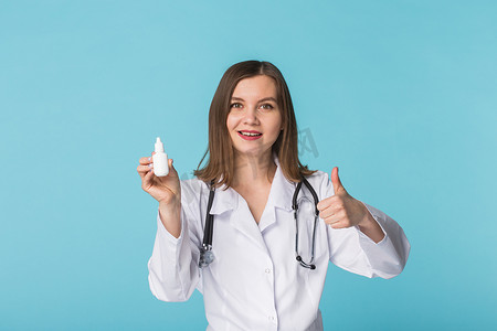 药物和药物概念 — 蓝色背景中竖起大拇指的年轻女医生或药剂师拿着鼻腔喷雾剂