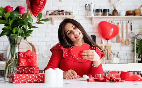 气球情书摄影照片_穿着红色裙子的年轻浪漫女人坐在装饰精美的厨房里写情书