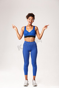 全长兴奋而快乐的非洲裔美国健身女孩，穿着蓝色运动服，指向侧面，显示左右标志，脸上高兴，白色背景
