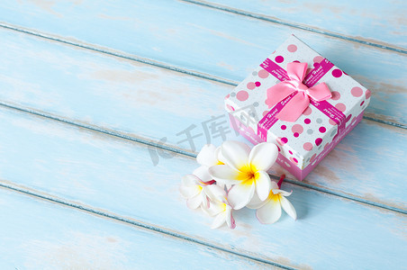 天蓝色木地板上有鲜花的粉色礼品盒。