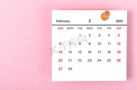 2022 年 2 月日历卡和粉红色背景的木制图钉。