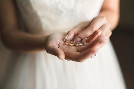穿着白色连衣裙的新娘手里拿着金色的结婚戒指。