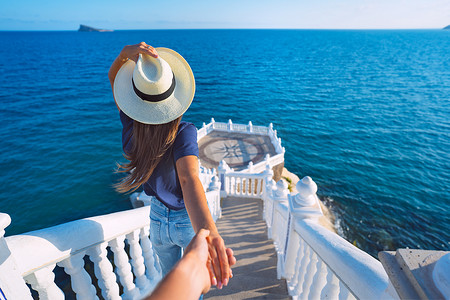 城市海景摄影照片_戴着帽子的无忧无虑的旅游女人带领她的男朋友去海景。