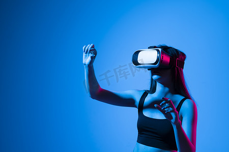 身穿黑色 T 恤、头戴 VR 耳机的黑发女性在玩游戏或观看 3d 电影时抬头看着虚拟现实中的物体，并试图触摸它。