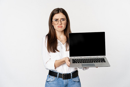 悲伤的黑发女孩，学生展示笔记本电脑屏幕，表情沮丧，在白色背景下失望地站着