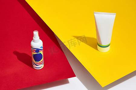 白色表面上方的红色和黄色纸上没有标志的彩色化妆品管和泵瓶。