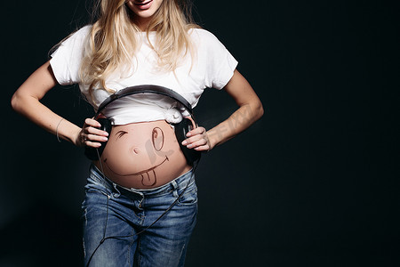 肚子大摄影照片_微笑的怀孕女性肚子上戴着大耳机。