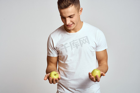 一个手拿苹果的男人，背景浅，身穿白色 T 恤，双手微笑着指手画脚