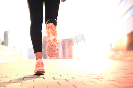 跑步者的脚在路上奔跑，特写在鞋子上，在城市的日落或日出时在户外