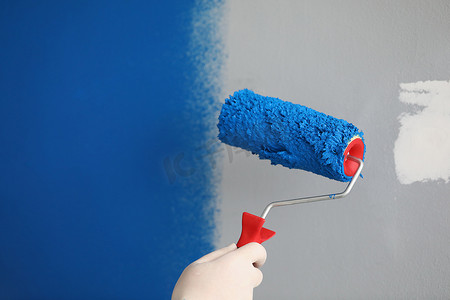 工人用滚筒工具准备粉刷墙壁，用蓝色覆盖