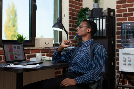 非洲裔美国企业家用笔摸下巴，看着笔记本电脑屏幕