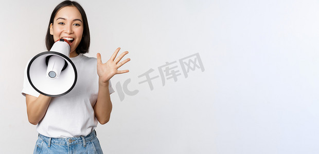 快乐的亚洲女人对着扩音器大喊大叫，发布公告，做广告，站在白色背景上