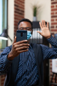 初创公司员工戴着口罩在在线采访中挥手打招呼的智能手机特写