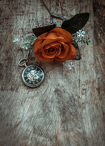 创意木板背景摄影照片_橙色玫瑰花和旧木板背景上的复古怀表。