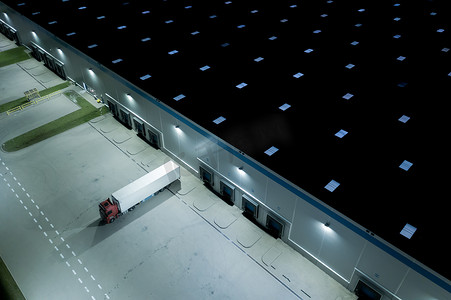 在 Logostics 中心卸载卡车和货物拖车的夜间空中俯视图。