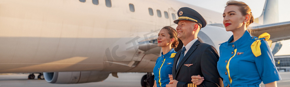 日落时分，兴奋的男飞行员和两名身穿蓝色制服的空乘人员在航站楼的飞机前行走