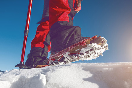 高端装备摄影照片_冬天穿着雪鞋和鞋钉在雪地上行走的视图。
