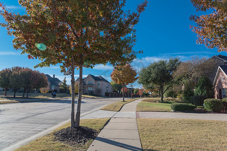 落叶街道摄影照片_美国德克萨斯州达拉斯郊区，干净的街区街道上有色彩缤纷的秋叶和不明身份的人早上散步
