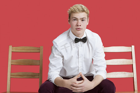 红色背景中坐在椅子上的一位身穿正装的英俊年轻人的肖像