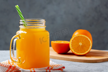 饮料吸管摄影照片_用橙子新鲜制作的柑橘汁，装在罐子杯里，灰桌上放着吸管