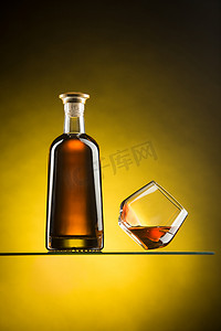 静物画中有一瓶烈酒和一个漂浮在带有黄色西耶娜渐变斑点背景的玻璃表面上的玻璃杯。