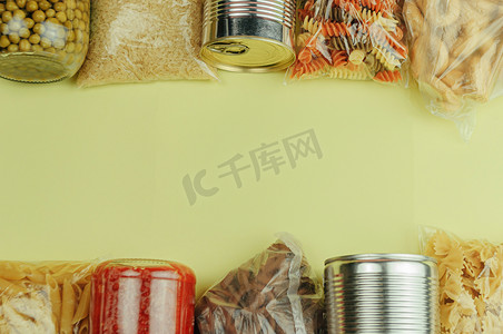 黄色背景顶视图中的一组产品，包括面食、米饭、饼干、番茄酱、豌豆和罐头食品。