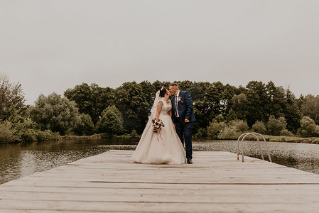 新婚夫妇在湖上的木墩桥上亲吻拥抱