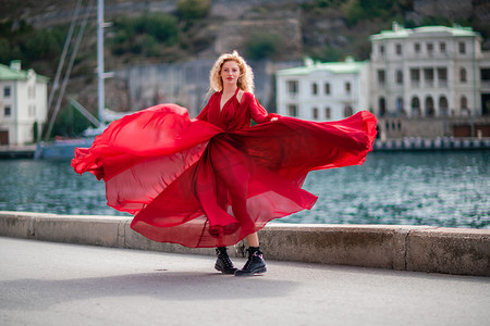 红堤摄影照片_身着红裙的女子，长着丝绸长翅膀的时装模特，身着飘逸的裙子，在堤岸上飞舞着布料。