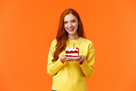 女朋友举办了惊喜派对，带了一块蛋糕和一根蜡烛来庆祝伴侣的生日，唱着快乐的生日，微笑着可爱，穿着黄色毛衣站在橙色背景