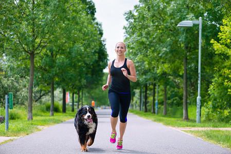 户外运动 — 年轻女子在公园里和狗一起跑步