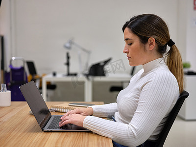 一位有进取心的女性在桌面上使用电脑的侧视图