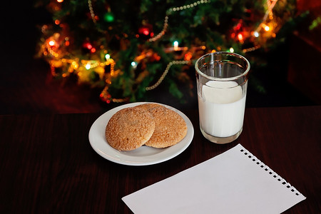 饮料和点心摄影照片_圣诞饼干和牛奶，附有灯光前圣诞老人的便条