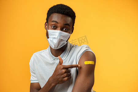 接种疫苗的非洲裔美国人在黄色背景下展示他的手臂