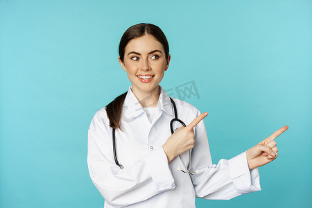 年轻专业医生、女医院工作人员的肖像，右指，展示标志，诊所促销交易，站在绿松石背景上