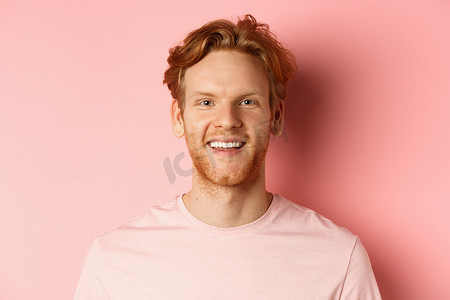 鼠年国潮背景摄影照片_留着胡须和洁白牙齿的快乐红头发男人的头像，他对着镜头微笑，站在粉红色背景上