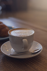 拿铁咖啡摄影照片_关闭热卡布奇诺咖啡，桌上的拿铁咖啡，咖啡店背景模糊。