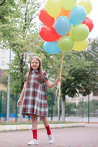 方格彩色摄影照片_迷人的少女穿着格子棕色连衣裙，带着一堆彩色气球。